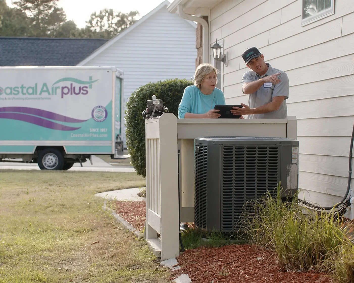 Coastal Air Plus technician reviewing a new HVAC system with a homeowner beside an outdoor unit